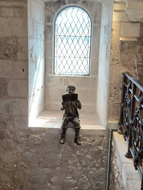 Escultura de bronce de un niño sentado leyendo un libro
