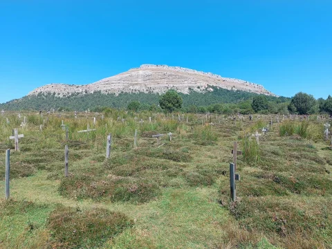 Cruces de madera en el prado del Cementerio de Sad Hill bajo un cielo azul despejado con las Peñas de Carazo al fondo