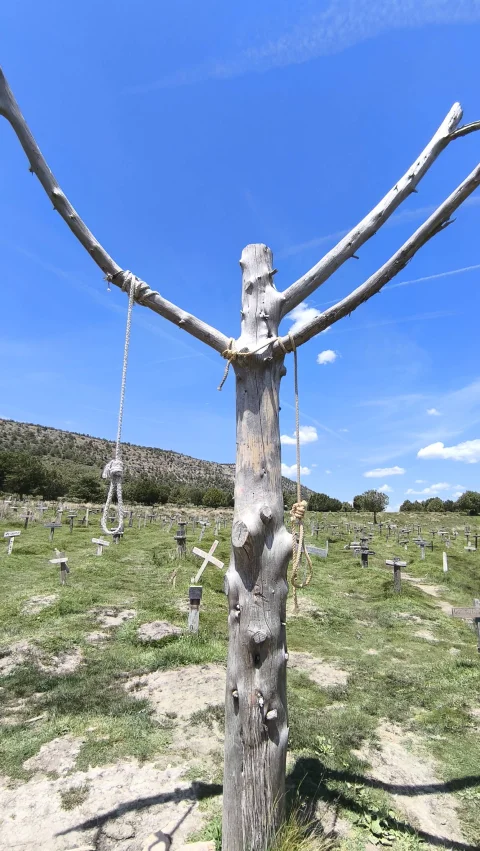 Árbol seco central con sogas colgando de las ramas frente a las cruces del Cementerio de Sad Hill bajo un cielo azul despejado