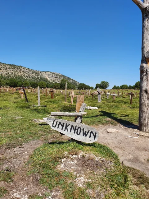 Primer plano del cartel de la tumba Unknown El Desconocido con el mar de cruces y colinas de fondo en el Cementerio de Sad Hill