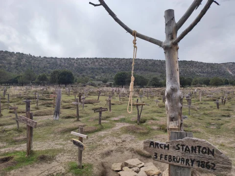 Tumba de Arch Stanton con soga colgando del árbol central y mar de cruces en el Cementerio de Sad Hill bajo cielo nublado