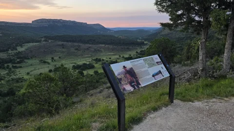 Panel informativo sobre la película El bueno, el feo y el malo en el Mirador de Sad Hill con vista panorámica del valle de Mirandilla al atardecer