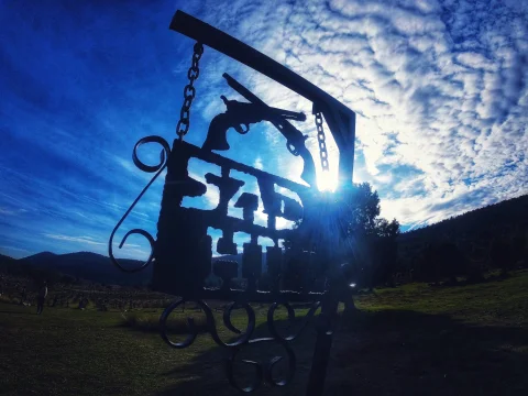 Letrero de forja de Sad Hill a contraluz con silueta de revólveres bajo un cielo azul con nubes