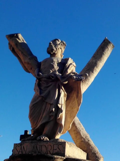 Estatua de piedra de San Andrés con su cruz en aspa sobre fondo de cielo azul