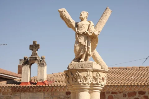 Primer plano de la escultura de San Andrés sobre columna de piedra con cruz en aspa