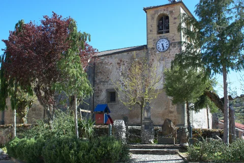 Fachada exterior y torre campanario con reloj de la Iglesia de Nuestra Señora de la Asunción rodeada de árboles