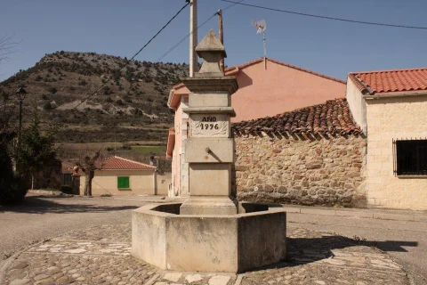 Fuente monumental de piedra con pilón hexagonal y fecha de 1996 en plaza de Contreras