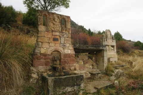Fuente rústica de piedra con caño y pilón junto al Monumento al Burro en entorno natural