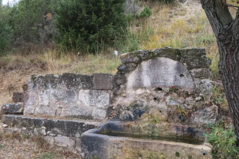 Fuente rústica de piedra con pilón rectangular y frontón con inscripciones grabadas en Contreras