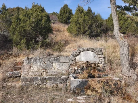 Fuente tradicional de piedra con banco y pilón en ladera con vegetación en Contreras