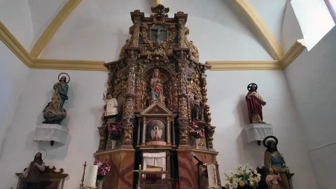 Retablo mayor barroco de madera dorada con imágenes religiosas en el presbiterio