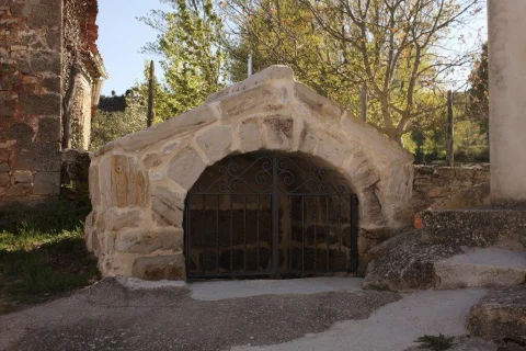 Estructura de piedra con arco y verja de forja que protege un manantial o fuente