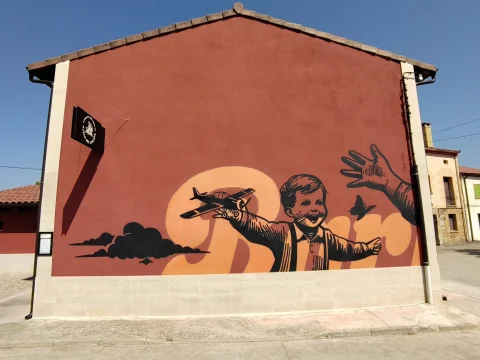 Mural exterior del Museo del Juguete que representa a un niño sonriente sosteniendo un avión de juguete