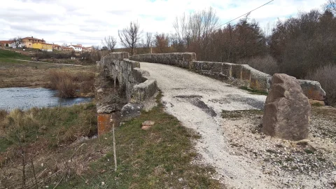 Calzada de tierra y pretil de piedra del Puente del Canto con el pueblo al fondo en Barbadillo