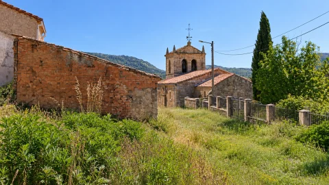 Torre campanario de la iglesia de Gete asomando tras muros de ladrillo y pradera verde