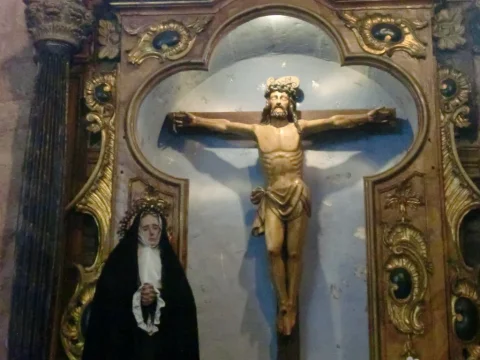 Talla de Cristo crucificado flanqueada por la Virgen de los Dolores vestida de luto en hornacina dorada