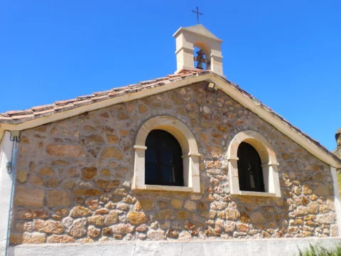 Fachada de piedra vista con dos ventanales de medio punto y espadaña en la ermita de San Roque