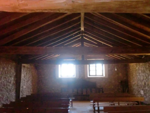 Nave interior de la ermita de San Roque con viguería de madera en el tejado y bancos de madera