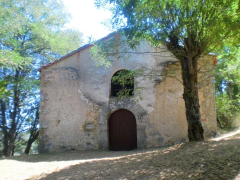 Portada y ventanal de medio punto en la fachada encalada de la Ermita de San Miguel junto a un árbol
