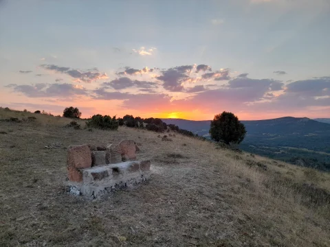 Banco rústico de piedra en lo alto de una loma contemplando el atardecer sobre los montes de Cervera