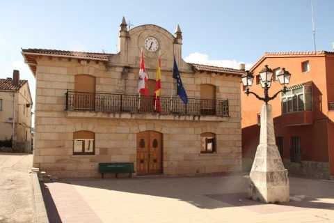 Fachada del ayuntamiento de Pinilla de los Barruecos con balcón de forja, banderas, reloj y farola de piedra