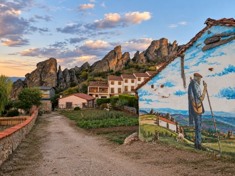 Pintura mural en fachada representando a un pastor con zurrón y vara frente a los riscos y casas del pueblo