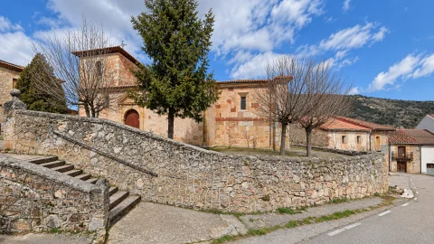 Acceso escalonado y muro curvo de mampostería frente a la iglesia de Santa Céntola en Mamolar bajo cielo con nubes