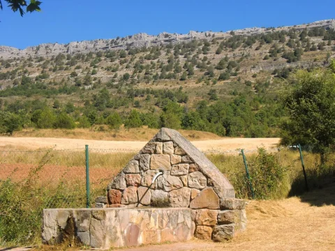 Fuente piramidal de mampostería de piedra con caño y pilón frente a loma arbolada en Mamolar