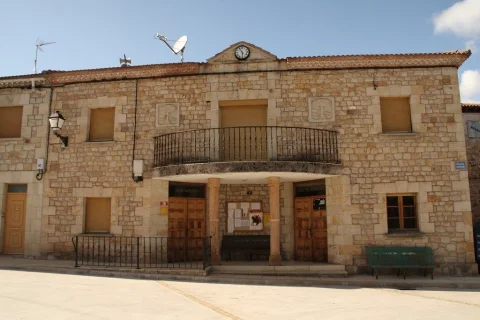 Edificio consistorial de piedra con soportal en la entrada, balcón corrido y reloj en el frontón de Mamolar