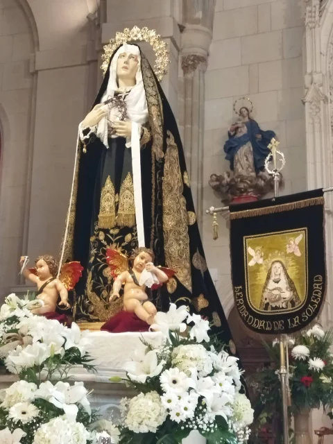 Escultura procesional de la Virgen de la Soledad vestida con manto bordado y arreglo floral en la Iglesia de Santa Águeda