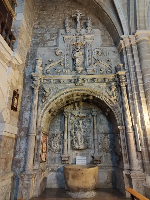 Pila bautismal de piedra frente a un retablo plateresco esculpido en la Iglesia de Santa Águeda de Burgos