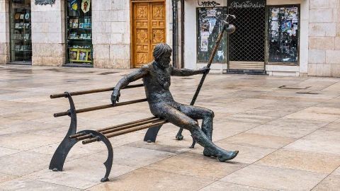 Estatua de bronce de un peregrino del Camino de Santiago sentado descansando en un banco de la plaza