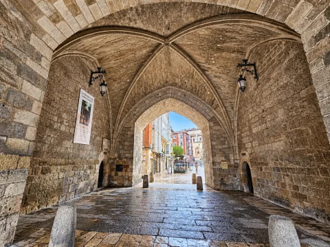 Perspectiva desde el pasadizo con bóveda de crucería de piedra hacia los edificios de la plaza catedralicia
