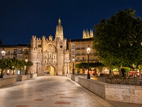 Vista nocturna iluminada del Puente y Arco de Santa María con la torre y cimborrio de la catedral al fondo