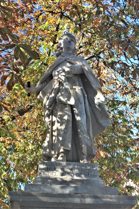Estatua de rey visigodo de piedra iluminada por el sol con fondo de densas hojas otoñales de castaño