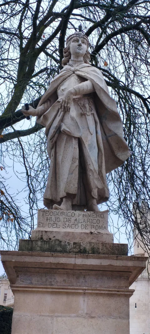 Vista frontal de la escultura de Teodorico I enmarcada por ramas invernales de plátanos de sombra