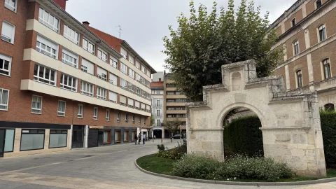 Arco monumental de piedra labrada sobre una zona ajardinada junto a una calle peatonal