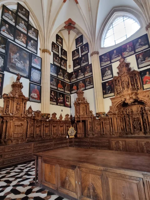 Mobiliario litúrgico de nogal tallado y paredes decoradas con retratos enmarcados de dignatarios eclesiásticos