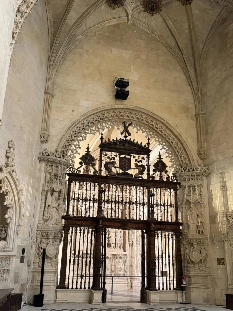 Monumental reja de hierro forjado y dorada bajo un arco gótico con decoración escultórica en piedra
