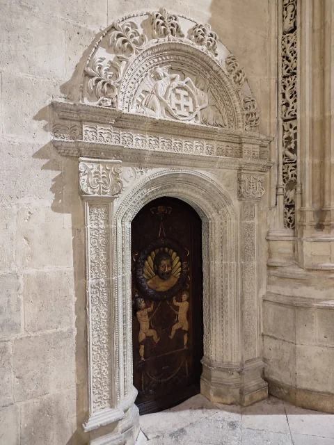Puerta renacentista de madera tallada bajo arco de piedra decorado con ángeles y escudo heráldico