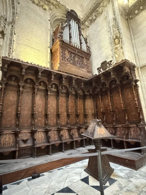 Sillería de coro de madera tallada con atril central y órgano barroco en la sacristía de la capilla