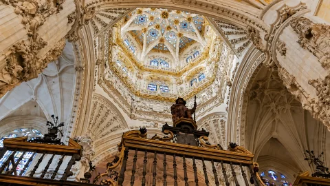 Torre linterna octogonal ricamente decorada en piedra blanca y dorados sobre una reja monumental de forja