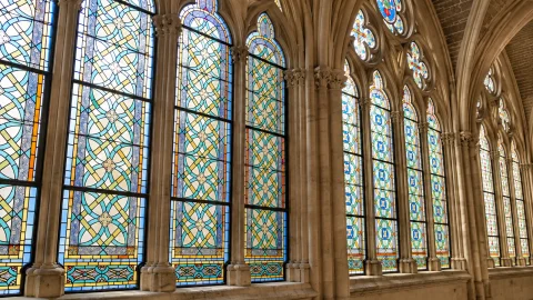 Detalle de ventanales apuntados con arquerías de piedra y vidrieras polícromas en tonos azules y amarillos