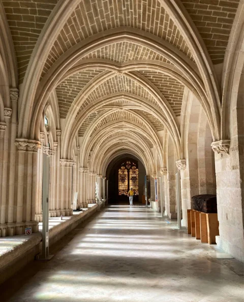 Galería claustral con bóvedas de crucería apuntadas y vidriera policromada al fondo en la Catedral de Burgos