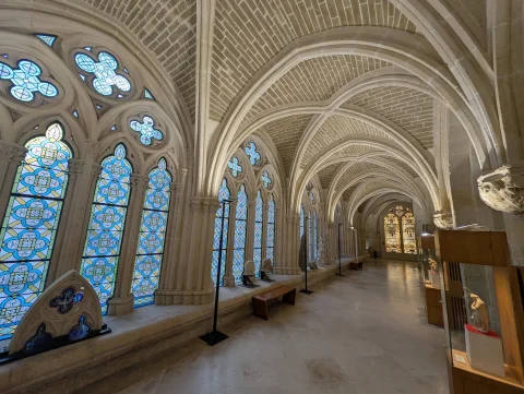 Galería gótica abovedada del Claustro Bajo con ventanales decorados con vidrieras y expositores de arte