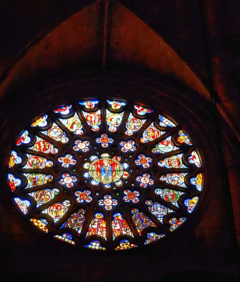Primer plano de rosetón gótico con vidrieras circulares de colores vivos y Cristo entronizado en el centro