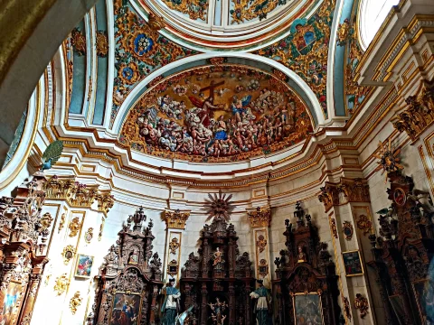 Interior de la sacristía barroca con retablos tallados de nogal bajo el relieve policromado de la Coronación y cúpula dorada