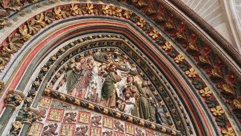 Detalle de tímpano gótico policromado con figuras en relieve del Descendimiento de Cristo y friso heráldico inferior