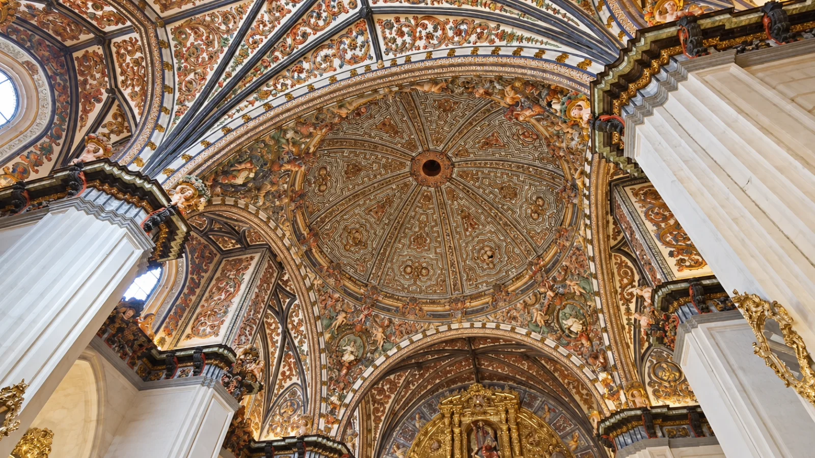 Cúpula semiesférica y bóvedas profusamente decoradas con yeserías barrocas polícromas y doradas