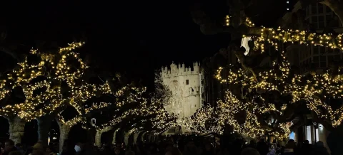 Iluminación navideña en las copas de los árboles con multitud de personas y el Arco al fondo